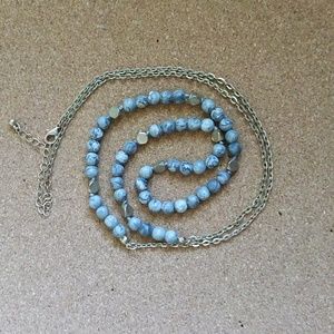 An opera length necklace with gray marbled beads, and gold geometric beads